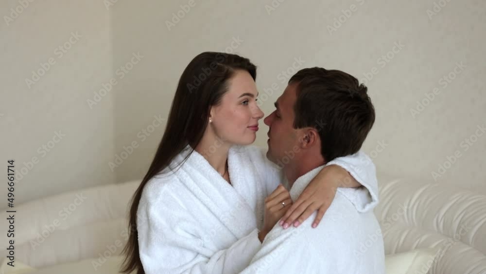 Ukrainian newlyweds sit on the bed and look at each other with love. Attractive handsome young man and woman wearing bathrobes are enjoying the morning in the bedroom at home. The concept of family Ukrainian newlyweds sit on the bed and look at each other with love. Attractive handsome young man and woman wearing bathrobes are enjoying the morning in the bedroom at home. The concept of family