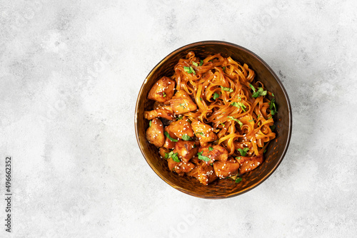 Udon noodles with chicken in teriyaki sauce in a brown bowl on a light gray culinary background. Top view from the copyspace