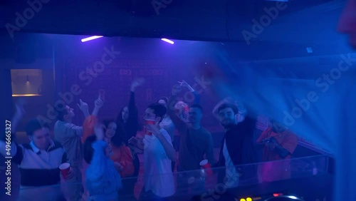 A crowd of people dancing on the dance floor of a nightclub under the light of colored spotlights. Night club photo