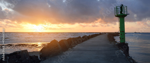 Old pier (walkway, promenade) to the lighthouse. Breakwaters close-up. Clear blue sky, pink sunset clouds, golden sunlight. Seascape, cloudscape. Baltic sea. Spring. Tourism, landmark, navigation photo