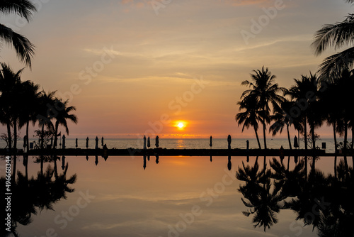 Sunset with swimming pool and sea on front and silhouette coconut tree