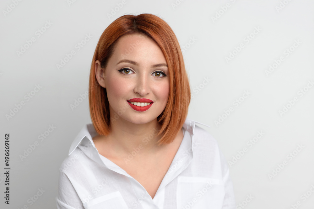 Beautiful happy smiling young redhead woman with bob haircut posing and looking at the camera. Portrait of an attractive girl with makeup and red lipstick in a casual shirt on a white background. Beautiful happy smiling young redhead woman with bob haircut posing and looking at the camera. Portrait of an attractive girl with makeup and red lipstick in a casual shirt on a white background.