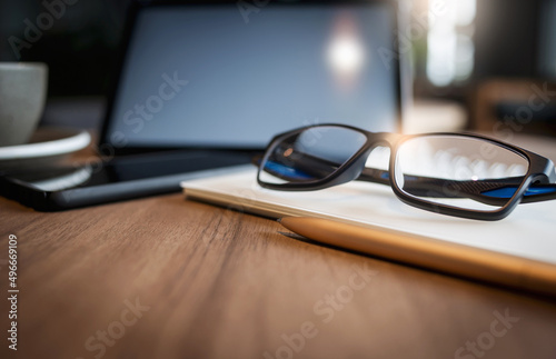 Work from home, desk office with digital tablet, blank notepad, eye glasses, on wooden table, close up and select focus on eye glasses