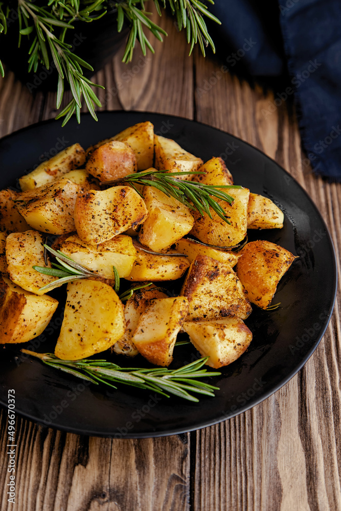 Baked potato slices on a black plate with rosemary branches with sauce on a rustic background. Baked potato slices on a black plate with rosemary branches with sauce on a rustic background.
