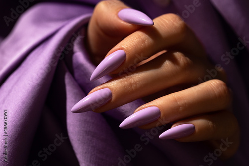 Girl's hand with an elegant manicure in a purple color on a purple silk background photo