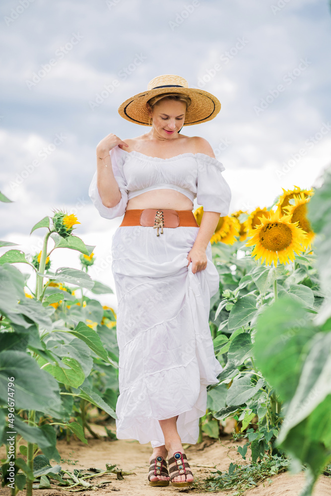 beautiful cute sexy girl in a white dress walks through the field of sunflowers