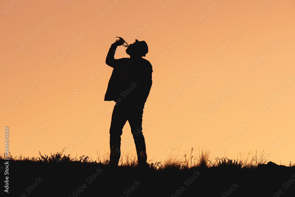 silhouette of man drinking water from bottle. man in hat stands and drinks water silhouette of man drinking water from bottle. man in hat stands and drinks water
