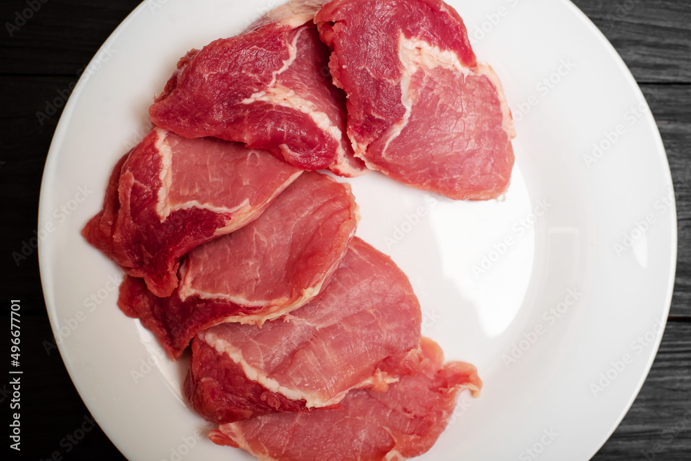Raw pork chop on a white plate on a black wooden background. Fatty meat beaten off for cooking. Raw pork chop on a white plate on a black wooden background. Fatty meat beaten off for cooking.