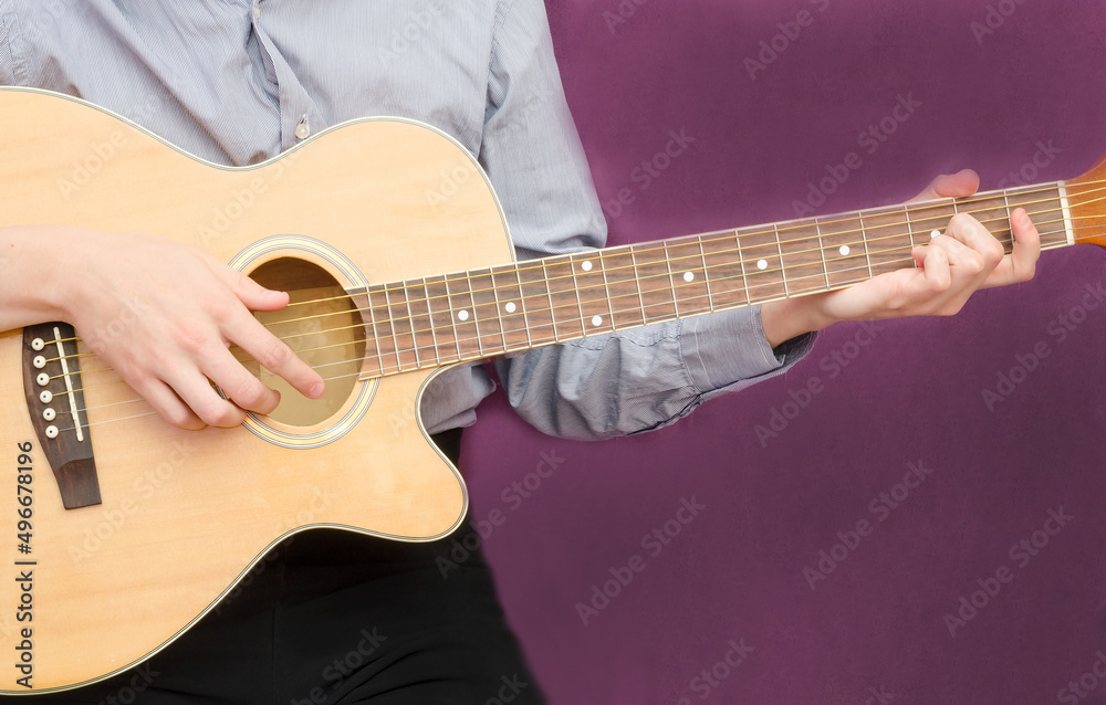 Young man playing guitar on dark purple background with copy space