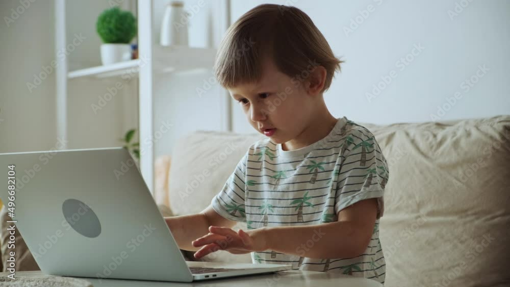 Happy child typing using laptop sitting on sofa at home, Homeschooling, remote education Happy child typing using laptop sitting on sofa at home, Homeschooling, remote education