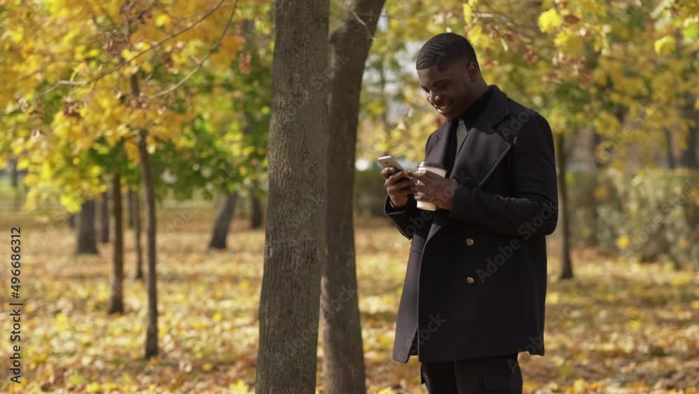 Phone messaging. Gadget communication. Mobile internet. Happy millennial man with coffee chatting on smartphone app at autumn forest empty space. Phone messaging. Gadget communication. Mobile internet. Happy millennial man with coffee chatting on smartphone app at autumn forest empty space.