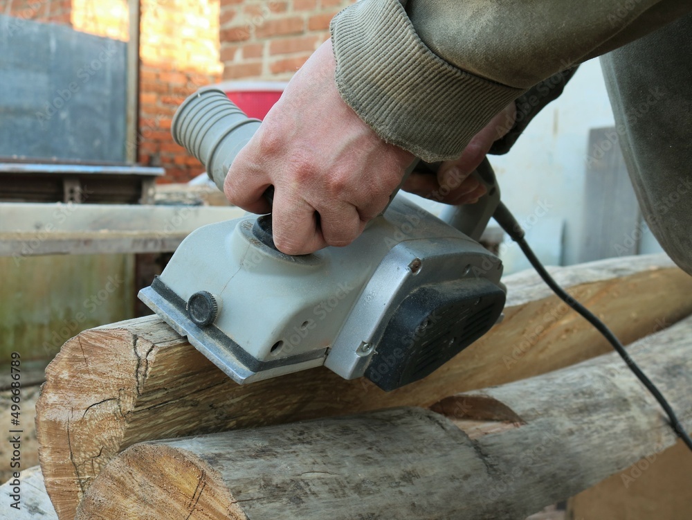 electric planer in the process of processing a whole dried log at a carpenter's workplace, cutting off the top texture and remaining bark from a long log, woodworking using an electric planer