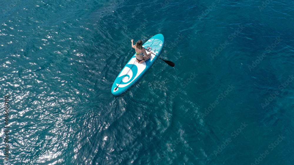 Aerial drone photo of fit unidentified woman paddling on a SUP board or Stand Up Paddle board in deep blue sea