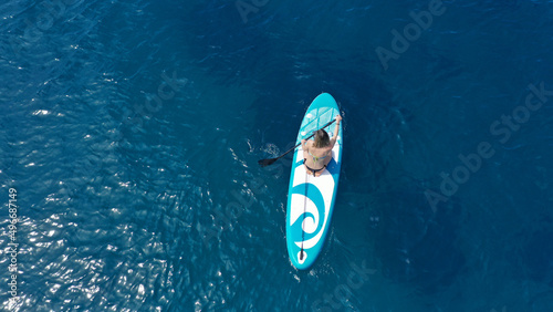 Aerial drone photo of fit unidentified woman paddling on a SUP board or Stand Up Paddle board in deep blue sea © aerial-drone