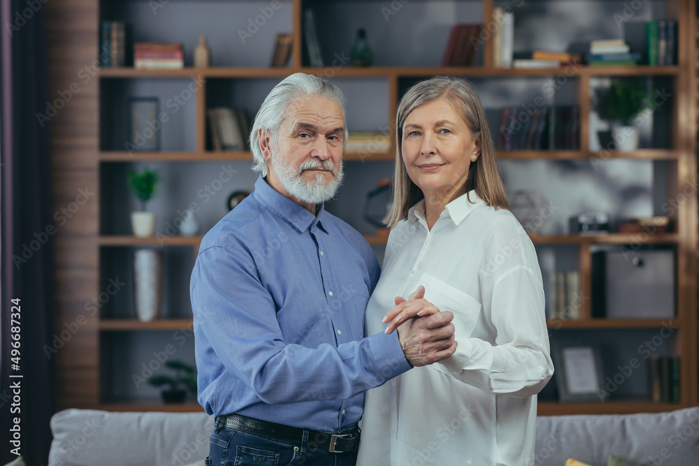 Obraz premium Happy married couple, gray-haired man and woman, smiling and looking at camera, hugging portrait at home