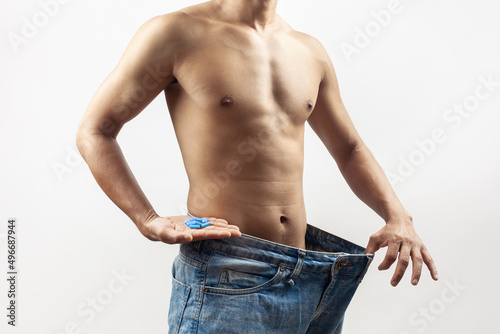 slim muscular fitness male wearing large jeans pant taking anabolic supplement pills