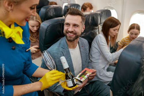 Stewardess giving champagne to man in passenger airplane