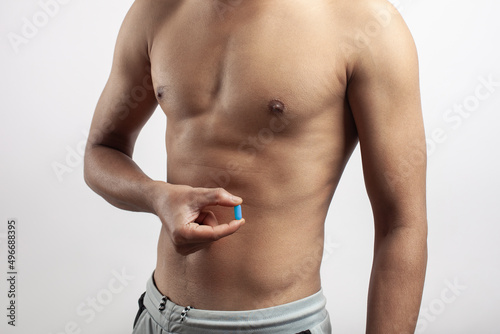 shirtless muscular man taking diet supplement pill