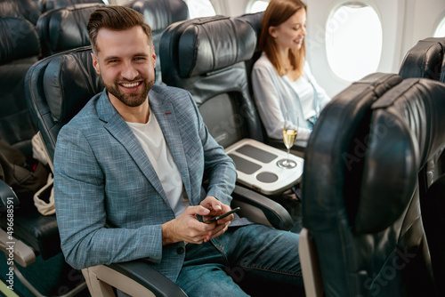 Cheerful bearded man using mobile phone in airplane