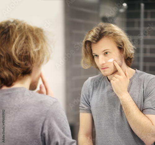 young man looking in the mirror combing his hair looking at problems on face.