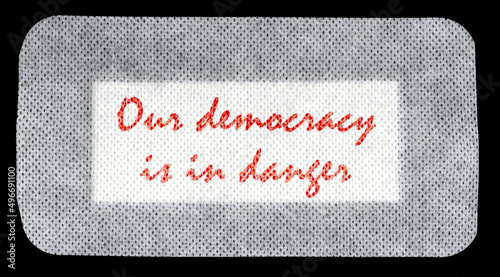 The words Our democracy is in danger, written with blood red ink on a big patch (a piece of medical material used to cover a wound).
