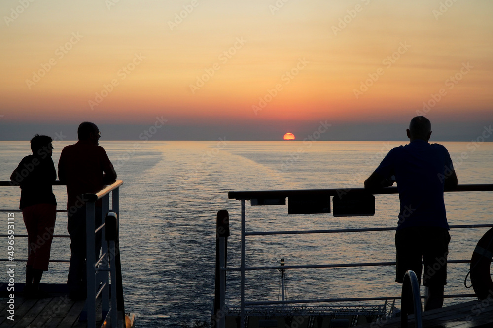 A golden sunset over the ocean watched by passengers on a cruise ship