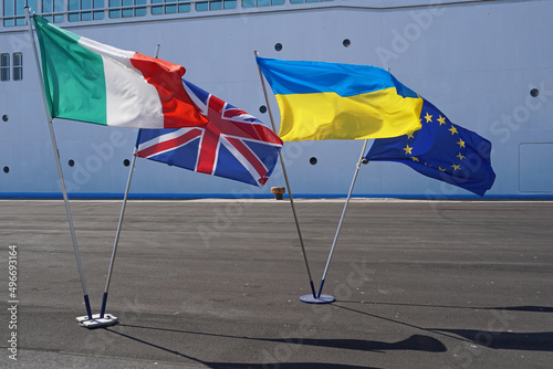 The national flags of Italy, The United Kingdom, Ukraine and the European Union displayed on a dockside with a cruise ship in the background photo