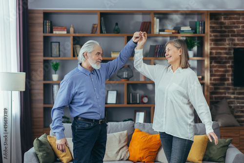 Happy cheerful senior married couple having fun at home. older family is dancing. Gray haired retirees rejoice moving active lifestyle. Old man and woman spend leisure time indoors listen to music