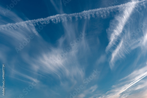 Die von Wind zerzausten Cirruswolken vor blauem Himmelshintergrund mit Kondensstreifen vorbeifliegender Flugzeuge