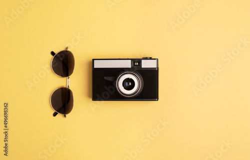 Retro camera and sunglasses on a bright yellow background. Flat lay, top view. 