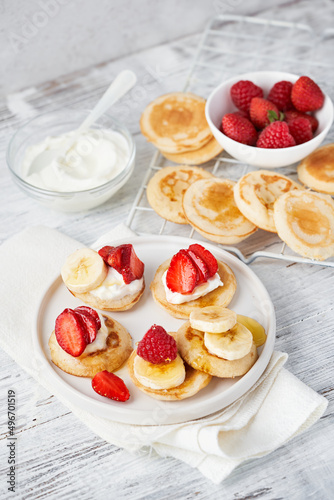 Mini pancake cereal with banana, raspberry, strawberry, honey, yogurt for breakfast. Mini pancake cereal is new trend. Mini pancakes cereal served for breakfast, snack. Selective focus, copy space.