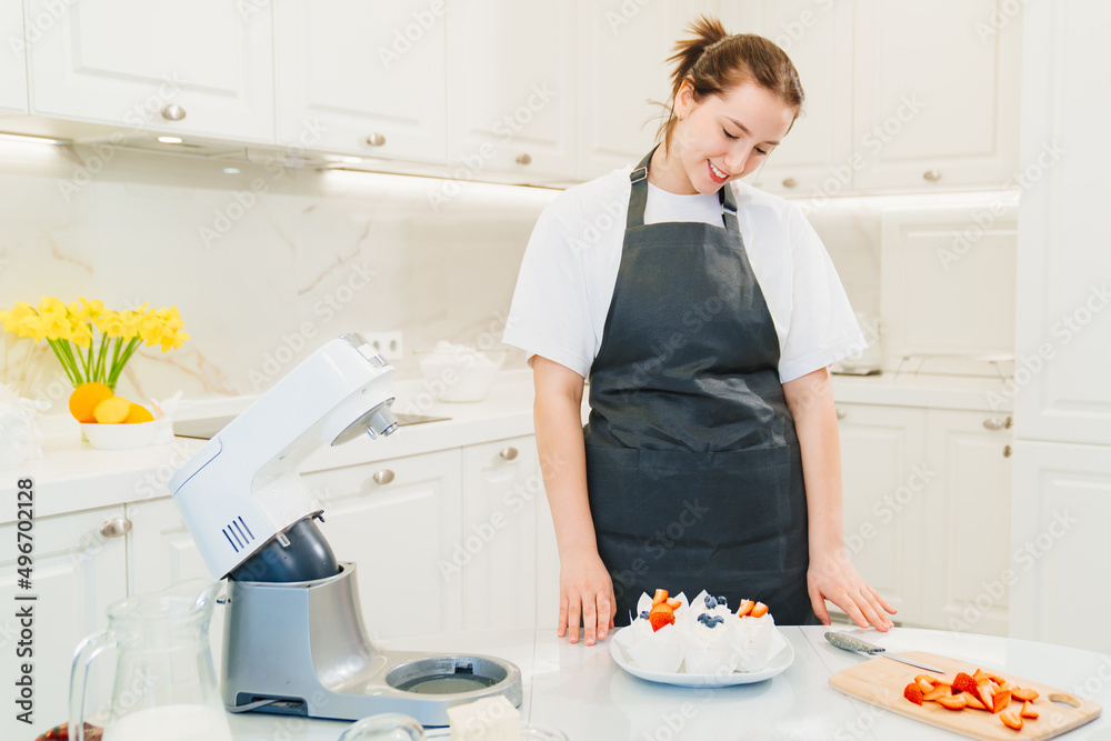 a young woman decorates cupcakes with white cream and fresh berries a young woman decorates cupcakes with white cream and fresh berries