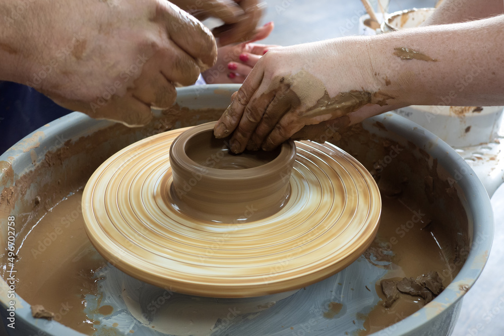 Fototapeta premium Woman potter teaching the art of pot making. Women working on potters wheel making clay objects. 