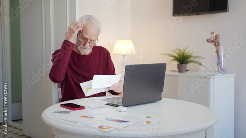 An elderly man pays taxes via the Internet. He scratches his head thoughtfully and examines bills