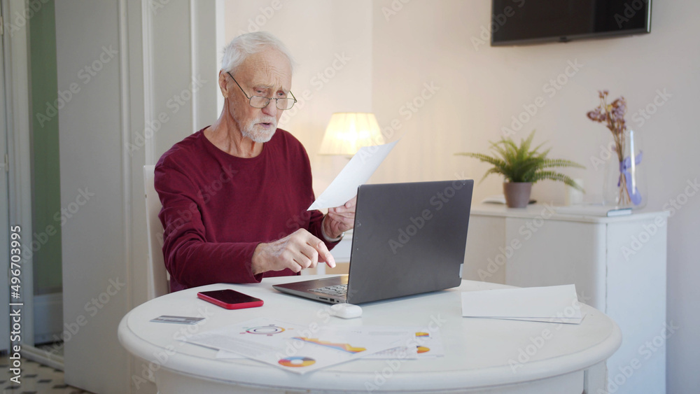 An elderly man is working on a laptop. He reviews documents and retypes them on the computer An elderly man is working on a laptop. He reviews documents and retypes them on the computer