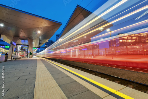 High speed train in motion on the railway station at night. Blurred red modern intercity passenger train  railway platform  buildings  city lights. Railroad in Vienna  Austria. Railway transportation