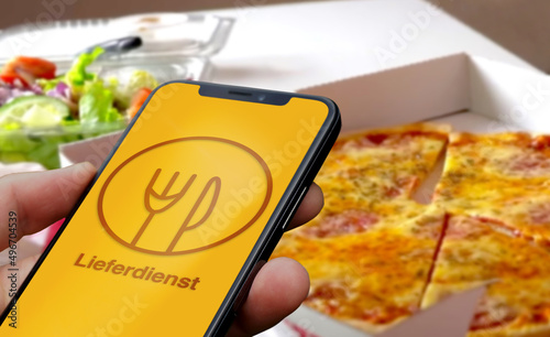 Person hält Smartphone mit einer fiktiven Lieferservice App vor einer gelieferten Pizza und Salat im Karton, Lieferdienst, Lieferservice, Essen, Gastronomie