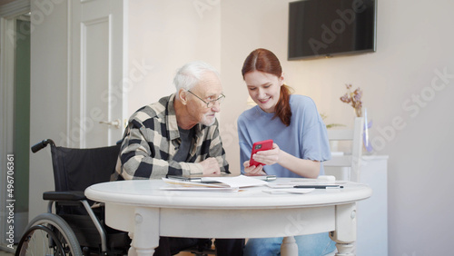 A woman tells an elderly man in a wheelchair how to use the phone