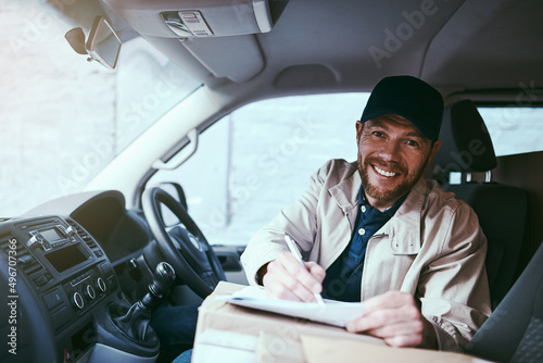 I have a few stops to make today. Portrait of a cheerful young delivery man seated in his car with boxes while signing on a digital tablet during the day.