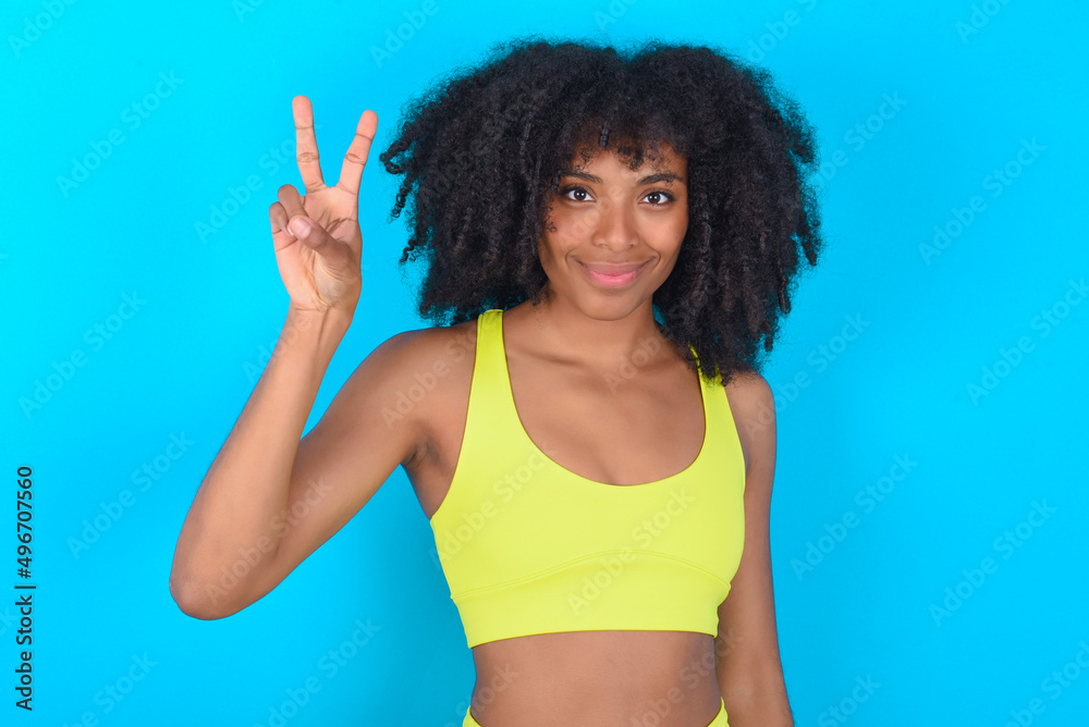 young woman with afro hairstyle in sportswear against blue background showing and pointing up with fingers number two while smiling confident and happy. young woman with afro hairstyle in sportswear against blue background showing and pointing up with fingers number two while smiling confident and happy.