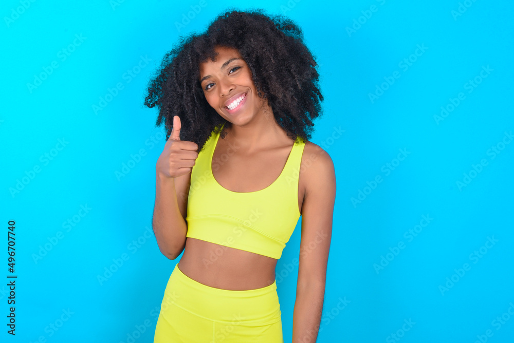 young woman with afro hairstyle in sportswear against blue background giving thumb up gesture, good Job! Positive human emotion facial expression body language. young woman with afro hairstyle in sportswear against blue background giving thumb up gesture, good Job! Positive human emotion facial expression body language.