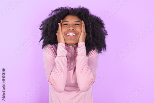young woman with afro hairstyle in technical sports shirt against purple background Pleasant looking cheerful, Happy reaction