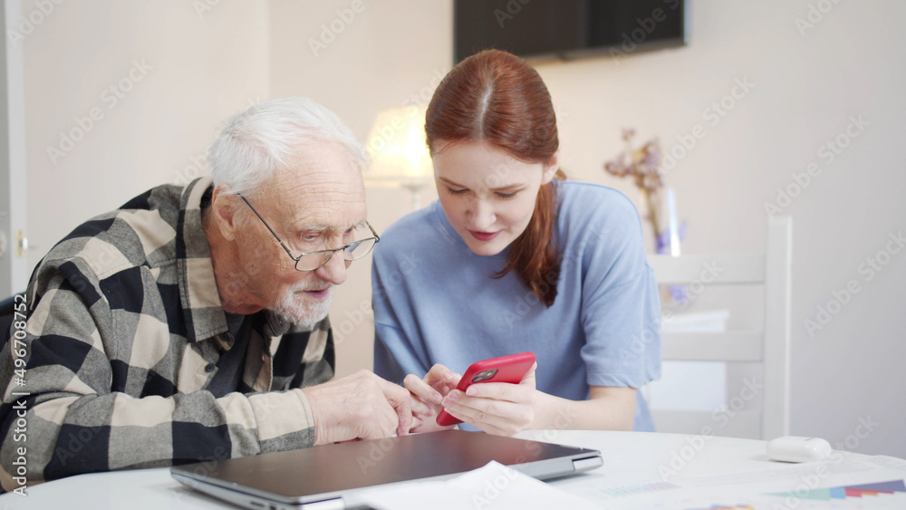 Grandpa is learning to use the phone. Social worker teaches pensioner Grandpa is learning to use the phone. Social worker teaches pensioner