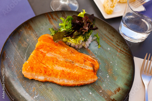 Salmon fillet with lettuce salad served on plate in restaurant.