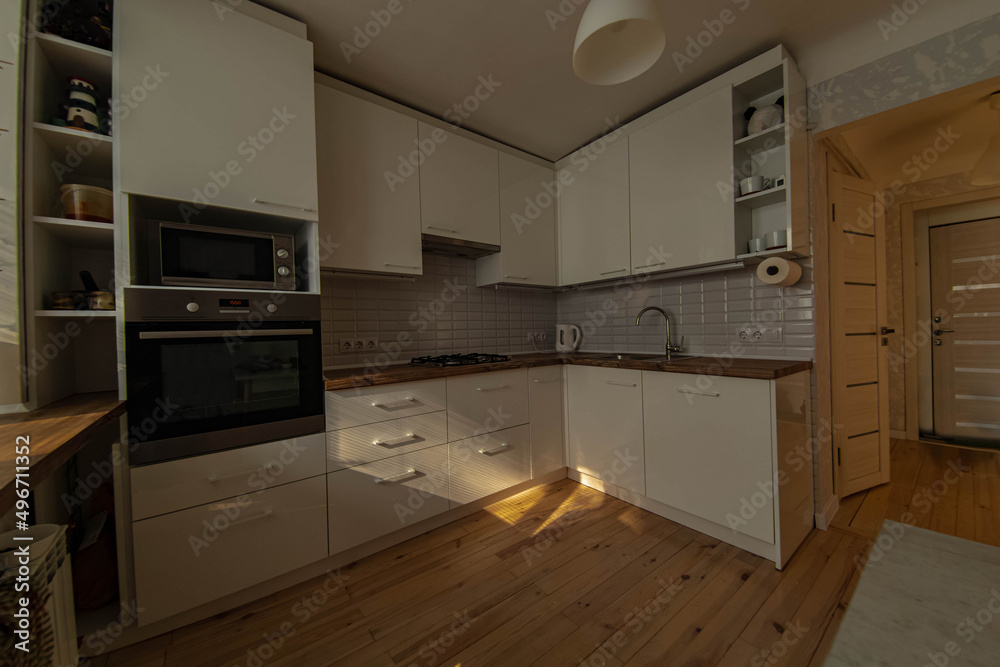 Fototapeta premium interior of a small cozy kitchen with wooden floor and white furniture, sunbeams in the room.