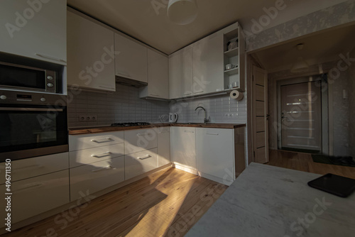 interior of a small sunny kitchen with wooden floor and white cabinets  solid wood worktop.