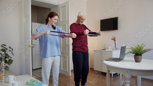 Grandfather and his adult daughter are engaged in exercises together. They use a fitness band
