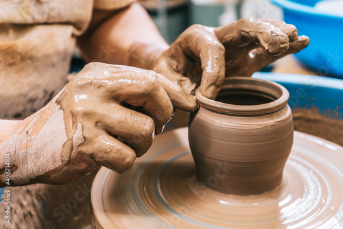 Hands of a potter working clay on a potter's wheel. The clay takes the shape the potter gives it with the terracotta tone of the clay.