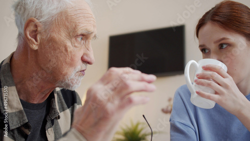 Woman volunteer communicates with an old man. They drink tea and talk