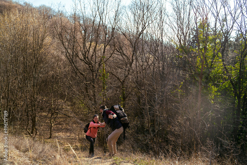 Man helping his girl to climb steep hill, hikers in nature